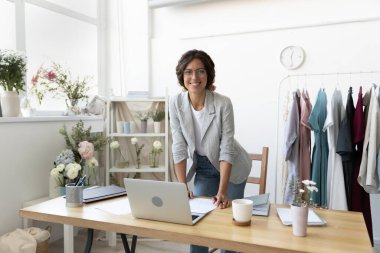 Gülümseyen genç beyaz kadın moda tasarımcısının portresi modern rahat ofis masasında poz veriyor. Mutlu kendine güvenen bin yıllık iş kadını stilisti veya terzisi yaratıcı iş yerinde çalışıyor..