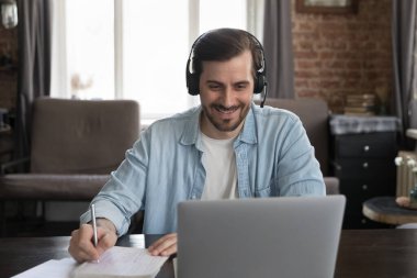 Milenyum dizüstü bilgisayar kullanıcısı kablosuz kulaklık takıyor, video görüşmeleri yapıyor, Webinar 'ı izliyor, notlar yazıyor. Yetişkin öğrenci internetten çalışıyor. Kablosuz iletişim kavramı