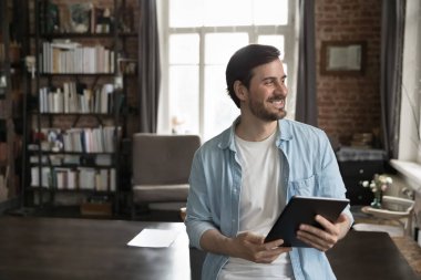 Gülümseyen iş adamı muhasebe ve finans ya da yönetim uygulamalarını dijital tablet üzerinde kullanıyor evde tek başına dikilip yan yana duruyor tatmin oluyor, rahatlıyor, kolay iş yapıyor modern teknoloji, iş akışı kavramı kullanıyor.