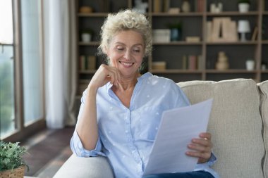 Gülümseyen orta yaşlı kadın mektupta hoş haberler okuyor, evde tek başına kanepeye oturuyor, bankadan kağıt tebligatı alıyor, kredi geri ödemesi, emekli maaşı zammı, yardım alıyor. Başarı, finans büyümesi