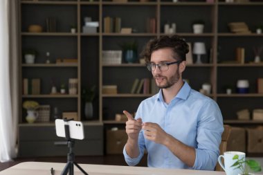 Sosyal medya ikonu, genç nüfuzlu adam akıllı telefon kamerasıyla vlog için yeni video kaydediyor, video görüşmelerine katılıyor, uygulamaları ve modern kablosuz teknolojileri kullanarak çevrimiçi çalışıyor. Günlük tutma