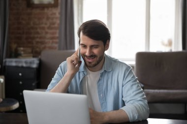 Mutlu nişanlı milenyum çalışanı ev telefonuna cevap veren, müşteriyle konuşan, cep telefonuyla konuşan, dizüstü bilgisayarda çalışan, gülümseyen.