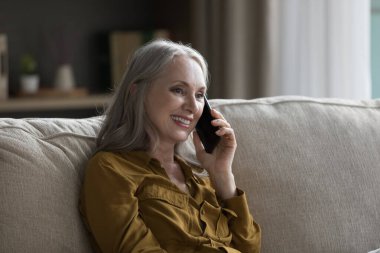 Mutlu, emekli yaşlı büyükanne kadın cep telefonuyla konuşuyor, koltukta oturuyor, konuşuyor, dinliyor, gülümsüyor, ailenle konuşmaktan keyif alıyor. İletişim konsepti