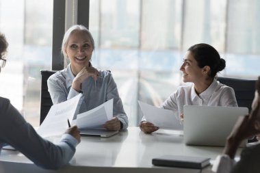 Başarılı çeşitli iş adamları proje üzerinde işbirliği yapıyor, istatistik raporlarını inceliyor, konferans masasında konuşuyor. Yetişkin kadın iş adamı, patron, akıl hocası eğitmen grubu.