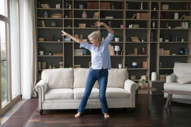 Geniş, modern oturma odasında yalın ayak dans eden, havalı şarkılar dinleyen, favori müziğe yönelen mutlu hisseden, evdeki sorunsuz emekliliğin tadını çıkaran yaşlı bir kadın. Boş zaman, hobi.