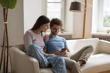 Mutlu, genç bir çift, kanepede birlikte oturuyor. Alet, internet uygulaması, cep telefonunda medya servisi, daktilo, ekrana bakıyor, gülüyor, gülüyor.