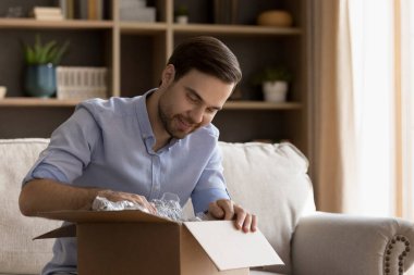 Meraklı genç erkek, postayla gelen iyi bir arkadaştan hediye paketini açıyor. İçine bak. Hoş bir sürprizin tadını çıkar. Mutlu milenyum insanları taşınma gününde yeni evlerinde eşyalarıyla birlikte kutuları açmaktan zevk alır.