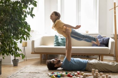 Neşeli heyecanlı sportif kız babasının desteğiyle uçakla oynuyor, gülümsüyor, gülüyor, güçlü babasının kollarında dengesini koruyor. Babacığın kızı kaldırıyor açık havada uçan elleriyle