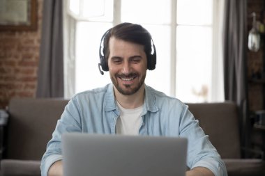 Gülümseyen genç iş adamı kulaklık takıyor ve modern ofisteki masada otururken video konferans aracılığıyla çevrimiçi iletişim kuruyor. Sanal toplantı, uzak danışmanlık ve danışmanlık konsepti