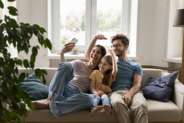 Mutlu, mutlu bir aile evdeki kanepeye selfie çekiyor, akıllı telefonlu koltukta dinleniyor, sarılıyor, gülüyor, el hareketleriyle gülüyor, çatı taklidi yapıyor.