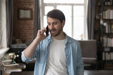 Engaged serious millennial business man in casual speaking on cellphone, talking on telephone call from home office, making order. Customer consulting support service, contact center