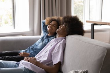 Güzel Afrikalı genç çift evlerinde kanepede oturup dinleniyor, modern evcil odada temiz havayı soluyor, sohbet ve zamandan keyif alıyor, ara veriyor, tasasız ve stressiz hissediyorlar.