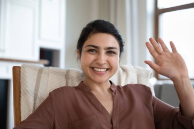 Kafa resmi, gülümseyen Hintli kadın internette el sallıyor sosyal ağda arkadaşlarıyla görüntülü konuşma yapıyor, evde sandalyeye oturuyor, genç bayanları selamlıyor, blog kaydediyor.