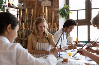 Çeşitli insanlardan oluşan bir atölye grubunda sanat terapisine katılan sanatsal stüdyo sınıfı, kağıda resim çizen boya fırçaları tutan, genç ve çekici sanatçı kadına odaklanan insanlar var. Eğitim, yaratıcı hobi kavramı