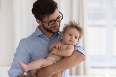 Genç 35 'lerin babası kucağında, yeni doğmuş bebeğini bebek beziyle kucaklıyor, rahat bir odada duruyor, oğluyla kızı arasında koşulsuz bir sevgi besliyor. Mutlu babalık, gelecek nesil, aile bağları konsepti.