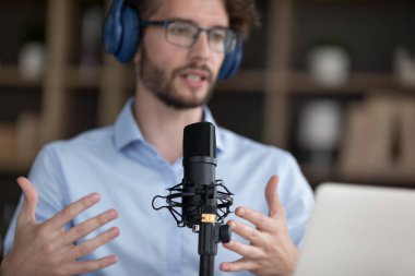 Yakından erkek mikrofona konuşma yapar, çevrimiçi görüşmelere öncülük eder, uzaktan iletişimde yer alır. Kulaklıklı adam konuşuyor, canlı sohbete katılıyor. Sosyal medya simgesi, etkili