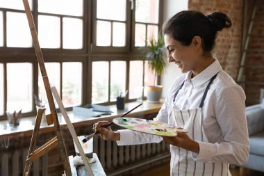 Şirin Hintli genç ressam kadın tuvalde resim yapıyor gülümseyen ressamlarla modern atölyede yaratıcı bir hobi sürecinin tadını çıkarıyor. Eğitim, yaratılış, ruh aktivitesi, yetenek kavramını geliştir
