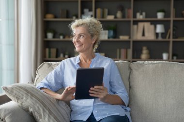 Elinde dijital tablet olan olgun, çekici bir kadın. Kafasını çevirmiş, modern aletlerle evde boş boş vakit geçiriyor. Rahat yaşamak için elektronik ticaret hizmetleri satın alıyor. Teknoloji, eğlence, eğlence.