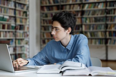 Öğrenci, özet ya da deneme üzerinde çalışıyor, sınavlarla meşgul, kitaplarla masada oturuyor, üniversite kütüphanesinde dizüstü bilgisayar kullanıyor. Genç nesil, yeni bilgi ve eğitim kavramı edinmek için modern teknolojiyi kullanıyor