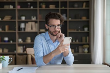 Düşünceli genç bir ofis çalışanı, iş adamı cep telefonu kullanıyor yeni cep telefonu uygulaması kullanıyor, mesaj okuyor, e-postayı kontrol ediyor, işten uzaklaştırılıyor internet üzerinden vakit geçiriyor, web sörfü yapıyor, teklif sunmayı öğreniyor.
