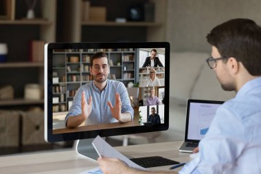Uzakta çalışan erkek şirket çalışanları, takım lideri meslektaşlarıyla sanal webcam konferans atölyesine katılıyor. Geri çekilen genç işadamı Webinar antrenmanını bilgisayar ekranından izliyor