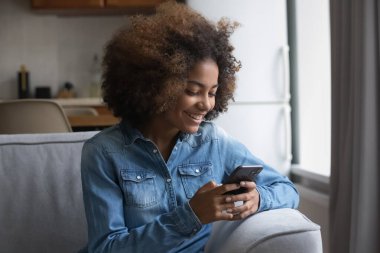 Afrikalı gençler kanepede cep telefonuyla oturuyor, kız arkadaşlarıyla mesajlarını sosyal medya üzerinden paylaşıyor, evde internet üzerinden modern teknoloji kullanıyor. Genç nesil aletleri eğlence ve iletişim için kullanıyor.