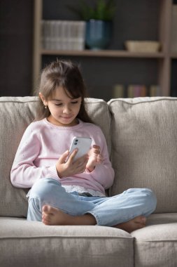Tatlı Latin kız rahat koltukta dinleniyor, haftasonunu oturma odasında cep telefonu kullanıyor, ekrana bakıyor, mesaj gönderiyor, yeni modern uygulamalar öğreniyor, evde online oyunlar oynuyor, internette geziniyor.