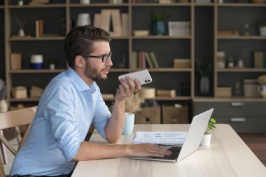 Gözlüklü genç adam çalışma masasında rahat bir ofiste oturuyor. Hoparlör kullanarak akıllı telefon konuşması yapıyor, sesli mesaj kaydediyor, işi uzaktan çözüyor, ofiste çalışan sesli mesaj gönderiyor.