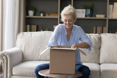 Mutlu, çekici, yaşlı bir kadın kanepede oturur, paketleri açar, gülümser, akrabalarından hediye alır, paketleri kontrol eder, beklenen mutlu bir paket olur, hızlı teslimattan memnun olur.