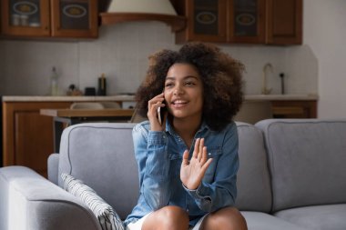 Güzel kıvırcık saçlı Afrikalı kız. Kanepede gevezelik ediyor. Akıllı telefonuyla konuşuyor. Özel sohbetin tadını çıkarıyor.