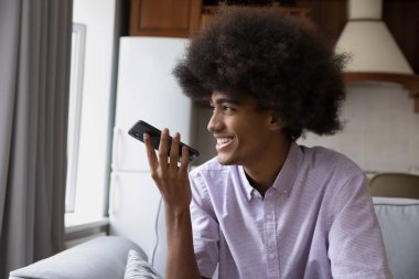 Yakışıklı 17 'li Afrikalı çocuk elinde akıllı bir telefonla kanepede oturuyor hoparlörden konuşuyor, gülüyor arkadaşınla uzaktan konuşmanın keyfini çıkarıyor, sesli mesaj bırakıyor, kız arkadaşına sesli mesaj gönderiyor uygulamayı kullanıyor.