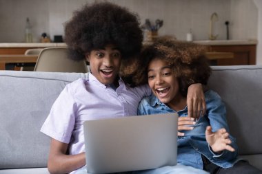 Surprised African teenagers couple gawp at laptop screen with mouths opened feel wondered, look amazed, receive fantastic commercial offer, sell-out, get huge discounts, read unbelievable media news clipart