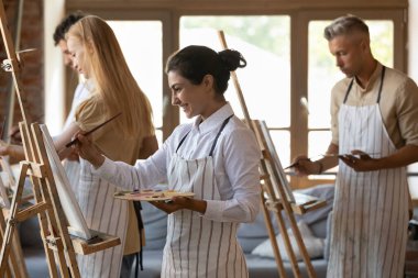 Çekici gülümseyen Hintli ressam kadın palet ve boya fırçasını modern stüdyodaki grup resim dersinde tuvale emerek yaratıcı bir hobiye katılıyor. Sanat okulu eğitim konsepti