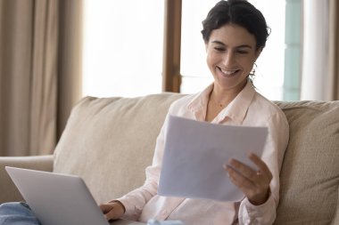 Gülümseyen genç kadın, dizüstü bilgisayarla koltukta oturan faturaları öderken son ipotek ödemesi hakkında bankacılık kağıdı bildirimi öğreniyor. Milenyum dişisi memnun oldu. Mektupta harika haberler okudu. Mutlu hissediyor.