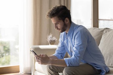 Milenyum sakallı ciddi bir adam evdeki koltukta oturan cep telefonunu kullanıyor. Bekar adam arama yapar, mesajları kontrol eder, mesajlara cevap verir, mobil uygulama kullanarak internette sohbet eder. Modern teknoloji, uzaktan iletişim.