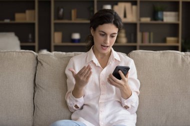 Kanepede oturan genç bir kadın akıllı telefon ekranına bakıyor kötü haberlerle mesajlar okuyor rahatsız oluyor, cihaz sorunları ile karşı karşıya kalıyor ve tatmin olmamış görünüyor. Cevapsız arama, bağlantı kesildi, uygulama veya telefon kazası kavramı