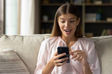 Genç kadın elinde akıllı telefonuyla kanepede oturur ekranda SMS 'i okurken afallar, inanılmaz ticari teklifler, harika haberler, büyük indirimler ve tüm biletler satılır. Piyango, açık artırma kazananı, şaşırtma konsepti