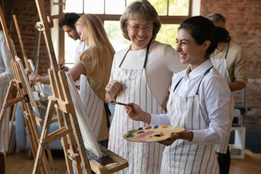 Sanat okulu öğrencisi ve büyük öğretmen resim dersi sırasında gülüyorlar. Hintli kadın palet tutuyor, resim sehpası yanında boya standı hobisinin, sanatsal pratiğin ve hocasıyla konuşmanın tadını çıkarıyor. Grup sanat sınıfı konsepti