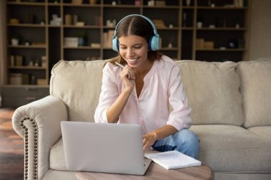 Genç ve güzel bir kadın evde bilgisayar kullanarak kulaklık takıyor, evde ders çalışıyor, ses sınıfını dinliyor, yabancı dil bilgisini geliştirerek kendini eğitmekle meşgul oluyor, özel öğretmenle ders alıyor. E-öğrenme konsepti