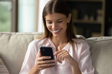 Akıllı telefon kullanarak güzel bir kadını yakından çek. Oturma odasındaki kanepede dinlenen gülümseyen kadın modern cep telefonlarını elinde tutuyor, mesajlarını paylaşıyor, arkadaşını arayıp evde zaman geçirtiyor. Teknoloji, yaşam tarzı konsepti