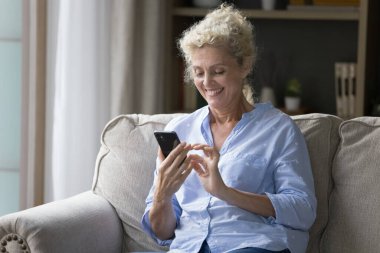 Mutlu yaşlı kadın akıllı telefonu tutuyor, mesajlar gönderiyor, SMS 'te haberleri paylaşıyor, internette aile veya arkadaşıyla sohbet ediyor, evde boş vakit geçiriyor, yeni mobil uygulamanın keyfini çıkarıyor, internette dinleniyor. Modern teknoloji