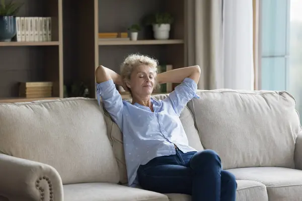 stock image Silent peaceful middle-aged woman take daytime break sit on couch in modern flat, enjoy fresh air-conditioned air inside cozy living room, daydreaming with eyes closed spend carefree leisure at home