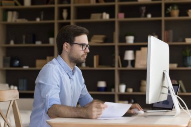 Meşgul erkek yönetici ofis bilgisayarlarında uygun profesyonel yazılım kullanarak finansal belgelerin satış artışını analiz ediyor. Çalışan genç bir erkek rutin hazırlık raporunu internetten doldurur.