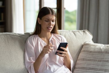 Genç kızgın kadın kanepede oturur akıllı telefon ekranlara bakar kötü haber, bozuk cihaz, kablosuz bağlantı kaybı, modern cihaz sorunu, mobil uygulama çökmesi konsepti yüzünden huzursuz hisseder.