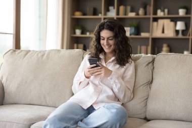 Çekici genç kız akıllı telefonuyla kanepede oturur. Genç gülümseyen bir kadın evde elinde modern cep telefonuyla vakit geçirir, arkadaşlarıyla mesajlaşır, e-randevu hizmetlerinden zevk alır, mesajlaşır. Teknoloji kavramı