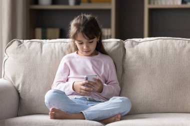 Küçük 6 'lılar, akıllı telefonlu Latin kız kanepede dinleniyor boş zamanlarını internette video ve karikatür izleyerek geçiriyor, yeni ve havalı mobil uygulamalar kullanarak. Genç nesil ve modern teknoloji aşırı kullanımı