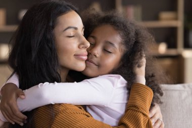 Barışçıl Afrikalı anne, tatlı küçük kızına kapalı gözlerle sarılıyor samimi bir okşama ve şefkat anının tadını çıkarıyor, saf koşulsuz sevgiyi hissediyor. Mutlu annelik, aile bağları kavramı