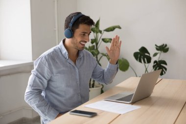 Kulaklık takan iş adamı ofiste masasında oturur video konferansı başlatır, dizüstü bilgisayar kullanır, iş görüşmeleri yapar, müşteriyle mesafeli görüşmeler yapar. Modern teknoloji, sanal buluşma konsepti