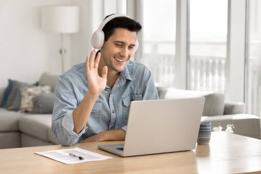 Neşeli, çekici, genç, İspanyol asıllı, kulaklıklı, bilgisayar konferansında konuşan, el sallayan, evde çalışan, internet iletişimini online öğrenim için kullanan profesyonel bir adam.