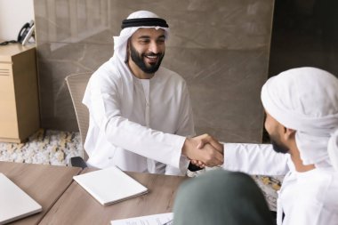 Beyaz kanduralı başarılı genç Arap girişimci, anlaşmadan sonra iş ortaklarıyla tokalaşıyor, gülümsüyor, gülüyor, anlaştığı için teşekkür ediyor.